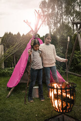 Two girls wearing feather headdress, with twist bread, looking into fire - MOEF01212