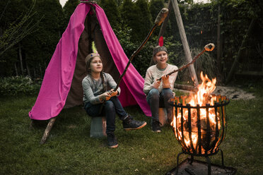 Zwei Mädchen mit Federkopfschmuck, mit Stockbrot am Lagerfeuer - MOEF01213