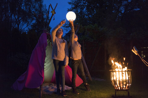 Two girls standing in front of tipi, holding lamp as moon stock photo