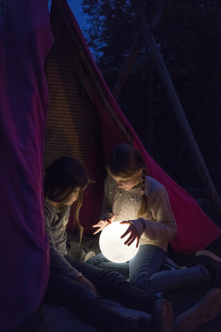 Two girls sitting in tipi, holding lamp as moon stock photo