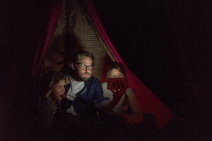 Vater und Töchter sitzen im Zelt und machen ein Selfie - MOEF01227