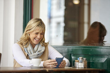 Mature woman reading smartphone text at sidewalk cafe table - CUF19439