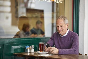 Mature man reading smartphone text at sidewalk cafe table - CUF19441