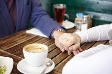 Close up of mature dating couple holding hands at sidewalk cafe table - CUF19449