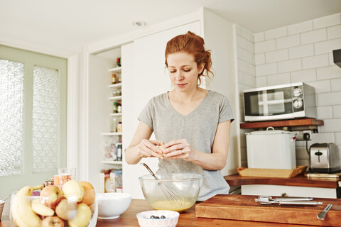 Mid adult woman cracking eggs at kitchen counter, lizenzfreies Stockfoto