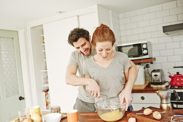 Mid adult couple whisking eggs together at kitchen counter for breakfast - CUF19541