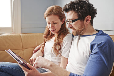 Mittleres erwachsenes Paar entspannt sich auf dem Sofa und schaut auf ein digitales Tablet - CUF19543