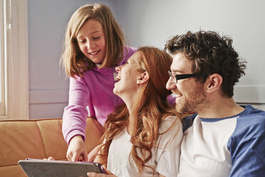 Eltern und Tochter auf dem Sofa mit Blick auf ein digitales Tablet - CUF19544