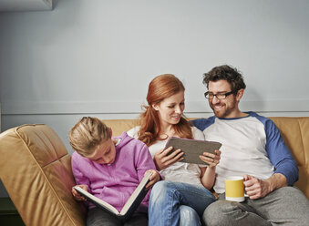 Mid Erwachsene Eltern und Tochter auf dem Sofa beim Lesen Buch und digitale Tablet - CUF19546