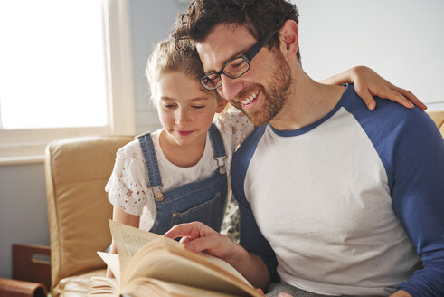 Mittlerer Erwachsener, der mit seiner Tochter auf dem Sofa ein Buch liest - CUF19549