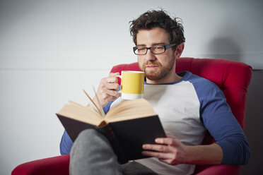 Mid adult man reading book on armchair - CUF19550