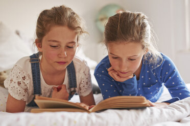 Two sisters lying on bed reading a book - CUF19552