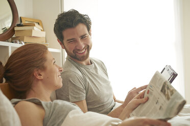 Mid adult couple reading broadsheet and digital tablet in bed - CUF19559