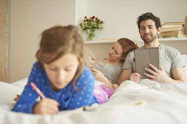 Mid adult couple having lie in while daughter draws on bed - CUF19563