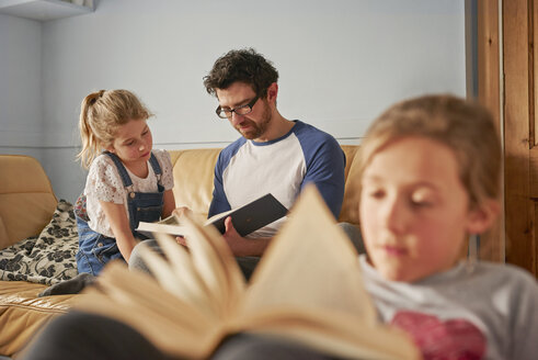 Mädchen, Schwester und Vater lesen Bücher im Wohnzimmer - CUF19585