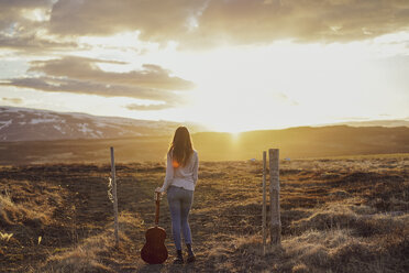 Island, junge Frau mit Gitarre bei Sonnenuntergang - AFVF00554