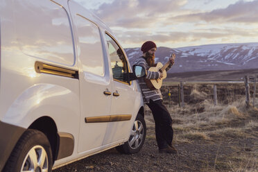 Island, junger Mann lehnt an Lieferwagen und spielt Gitarre - AFVF00560