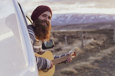 Island, junger Mann sitzt im Lieferwagen und spielt Gitarre - AFVF00562