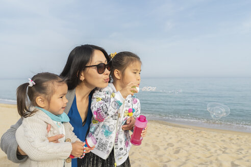 Mutter mit zwei Töchtern beim Seifenblasenblasen am Strand - AFVF00565