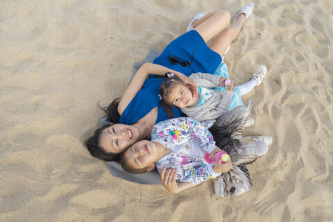 Happy mother with two daughters lying on the beach stock photo
