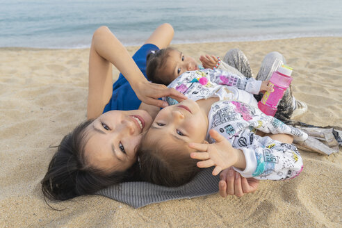 Glückliche Mutter mit zwei Töchtern am Strand liegend - AFVF00567