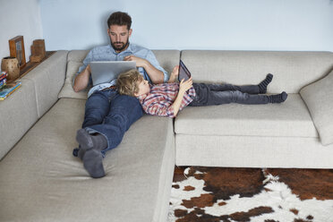 Junge auf dem Sofa liegend mit Vater, der Technik benutzt - CUF19603