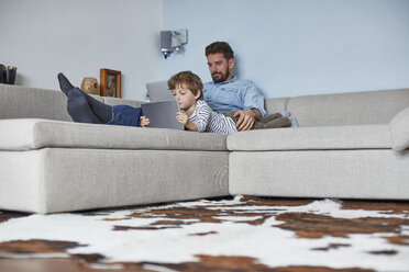 Boy lying on sofa with father using technology - CUF19605