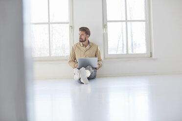 Young man sitting on floor with laptop in empty new home - CUF19614