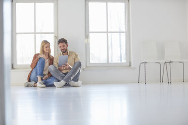 Couple sitting on floor browsing digital tablet in empty new home - CUF19616