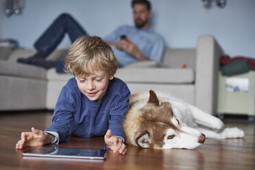 Boy lying on living room floor with husky using digital tablet - CUF19623