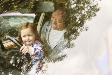 View through windscreen of daughter sitting on father lap driving car - CUF19650