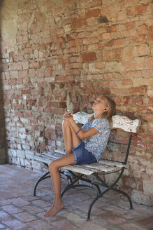 Mädchen sitzt auf einer Bank und hört Musik über Kopfhörer, Buonconvento, Toskana, Italien - CUF19661
