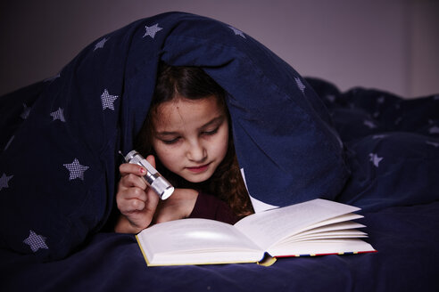 Girl underneath duvet reading book by torchlight - CUF19729