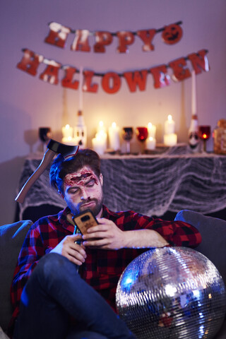 Gelangweilter Mann benutzt Handy auf Halloween-Party, lizenzfreies Stockfoto