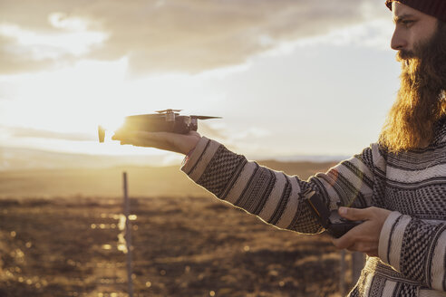 Island, bärtiger Mann, der bei Sonnenuntergang eine Drohne hält - AFVF00577