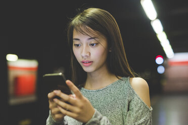 Young woman reading smartphone on railway platform at night - CUF19855