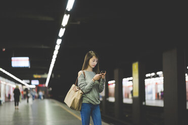 Junge Frau benutzt nachts ihr Smartphone auf dem Bahnsteig - CUF19858