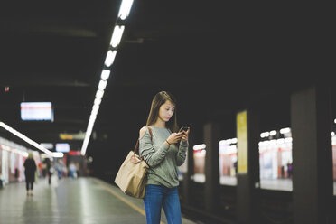 Young woman using smartphone on railway platform at night - CUF19858