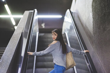 Portrait of young woman looking back from city escalator - CUF19859