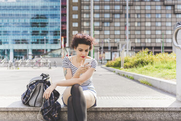 Woman sitting in urban area texting on smartphone, Milan, Italy - CUF19902