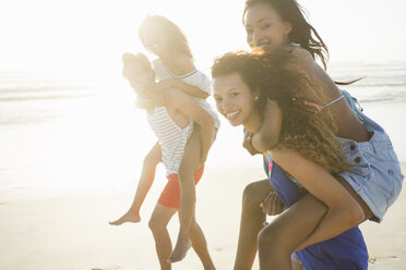 Young man and woman piggybacking friends in beach race, Cape Town, South Africa - CUF19916