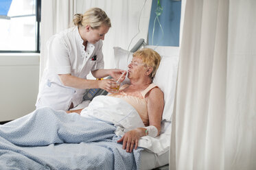 Krankenschwester hilft Patientin im Krankenhausbett beim Trinken - CUF19960