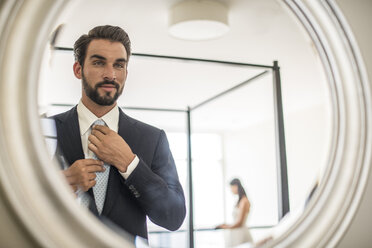 Mirror reflection of young businessman adjusting shirt and tie in hotel room, Dubai, United Arab Emirates - CUF19974