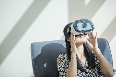 Frau auf Sessel schaut durch Virtual-Reality-Headset - CUF19984