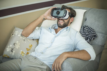 Young man on armchair looking through virtual reality headset - CUF19986