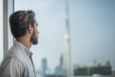 Businessman gazing through window with city view, Dubai, United Arab Emirates - CUF19992