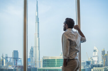 Geschäftsmann blickt durch ein Fenster mit Blick auf die Stadt, Dubai, Vereinigte Arabische Emirate - CUF19993