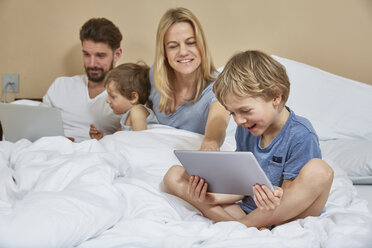 Mother and father in bed with sons using technology - CUF20029