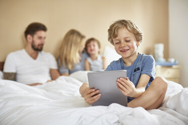 Junge auf dem Bett der Eltern mit digitalem Tablet, lächelnd - CUF20033