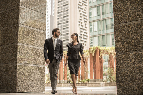 Geschäftsmann und Frau, die vor einem Büro spazieren gehen und sich unterhalten, Dubai, Vereinigte Arabische Emirate - CUF20056